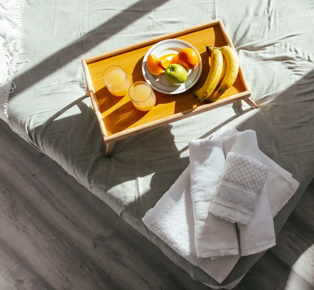 Bandeja de desayuno y toallas dobladas sobre la cama de un alojamiento