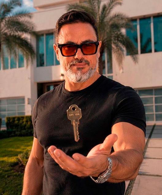 Alejandro Bernal entregando una llave frente a una casa moderna en Florida